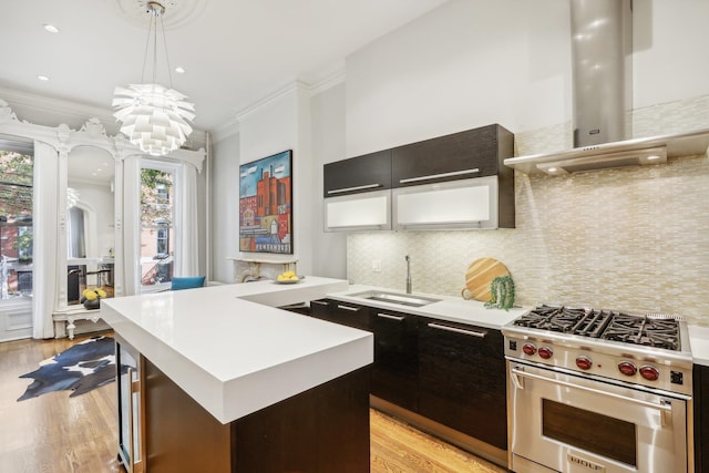 kitchen with light hardwood / wood-style floors, sink, wall chimney range hood, designer range, and decorative light fixtures