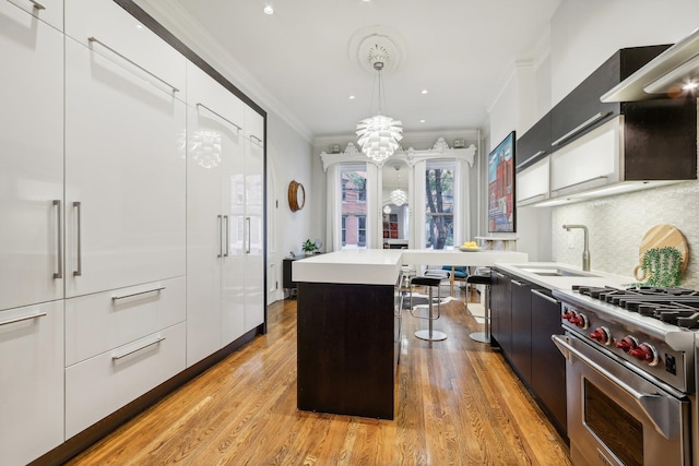 kitchen with crown molding, a kitchen island, hanging light fixtures, light hardwood / wood-style floors, and high end range