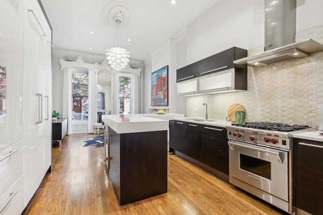 kitchen with wall chimney exhaust hood, designer range, hanging light fixtures, light hardwood / wood-style flooring, and a kitchen island