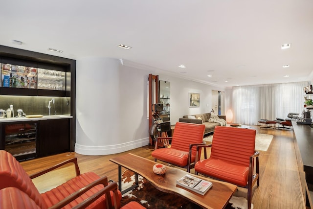 living room with light hardwood / wood-style floors, beverage cooler, crown molding, and wet bar