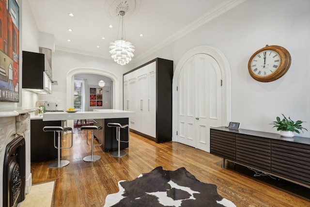 kitchen with decorative light fixtures, a kitchen bar, crown molding, and light hardwood / wood-style flooring