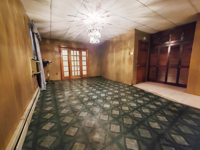 unfurnished room featuring a chandelier, wood walls, baseboard heating, and a drop ceiling