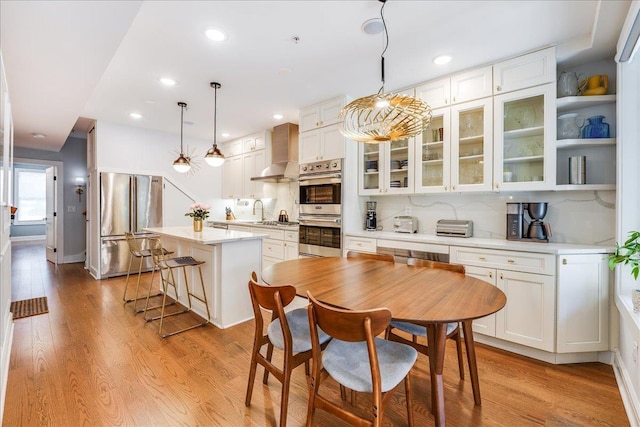 kitchen featuring light countertops, light wood-style flooring, appliances with stainless steel finishes, white cabinets, and wall chimney exhaust hood