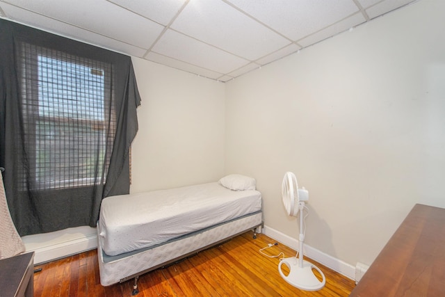 bedroom with a drop ceiling, baseboards, and wood finished floors