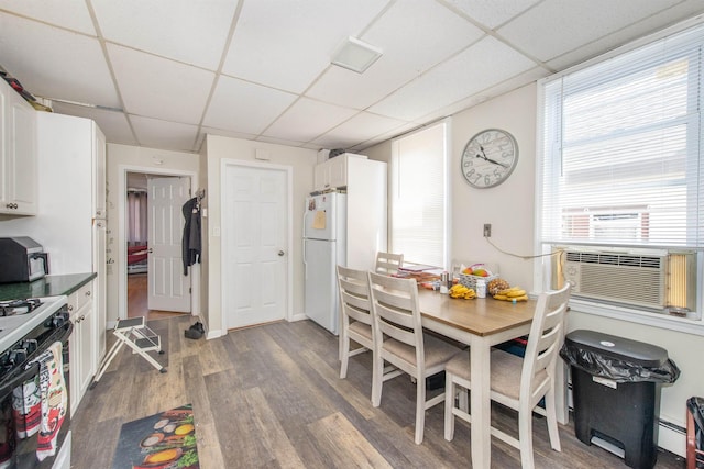 dining room with a baseboard heating unit, cooling unit, wood finished floors, and a paneled ceiling