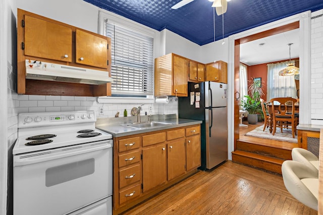 kitchen featuring decorative light fixtures, light hardwood / wood-style floors, white electric stove, stainless steel refrigerator, and sink