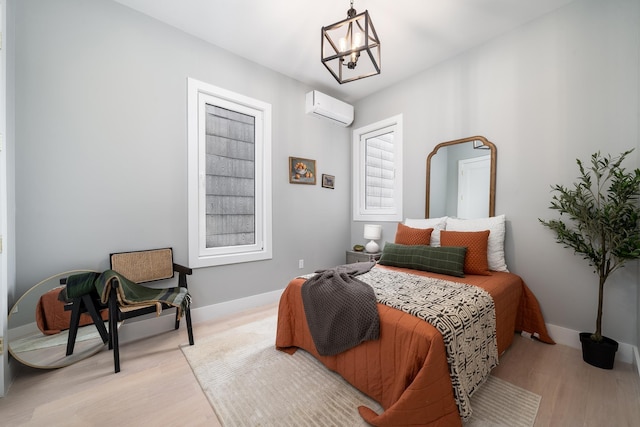 bedroom with an inviting chandelier, light hardwood / wood-style flooring, and a wall mounted AC