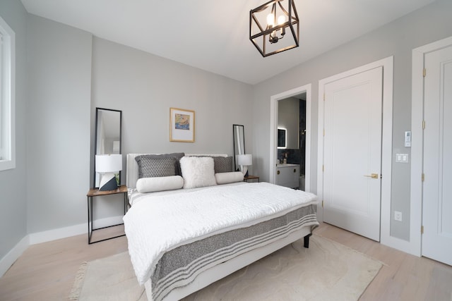 bedroom with light wood-type flooring, a notable chandelier, and connected bathroom