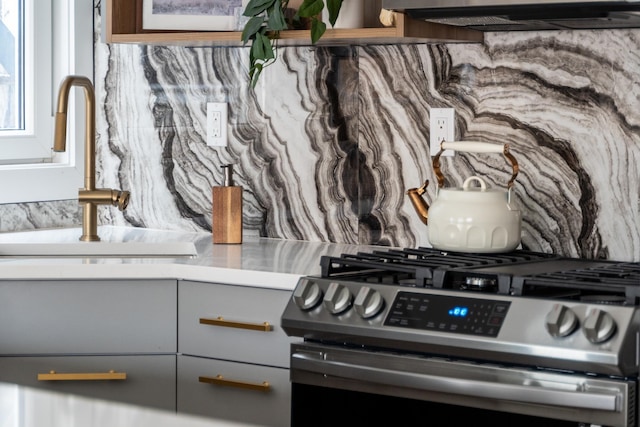 interior details with stainless steel gas range, exhaust hood, gray cabinetry, and sink