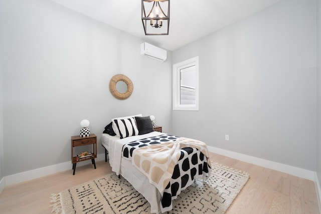 bedroom with a chandelier, light wood-type flooring, and a wall mounted air conditioner