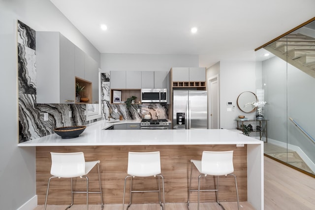 kitchen featuring kitchen peninsula, light hardwood / wood-style flooring, tasteful backsplash, appliances with stainless steel finishes, and a kitchen breakfast bar