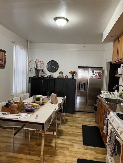 kitchen with stainless steel refrigerator with ice dispenser, dark countertops, gas range gas stove, a sink, and light wood-style floors