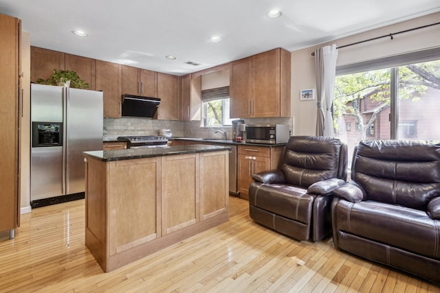 kitchen featuring decorative backsplash, under cabinet range hood, open floor plan, and appliances with stainless steel finishes