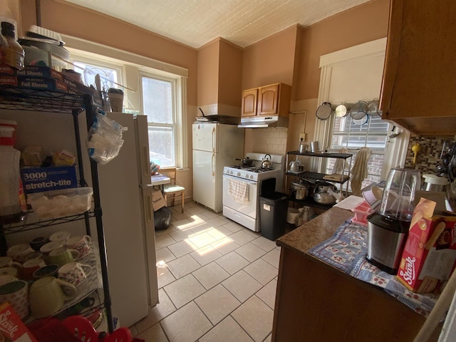143 64th St, West New York, NJ 07093 - kitchen featuring white appliances, under cabinet range hood, light tile patterned floors, dark countertops, and backsplash