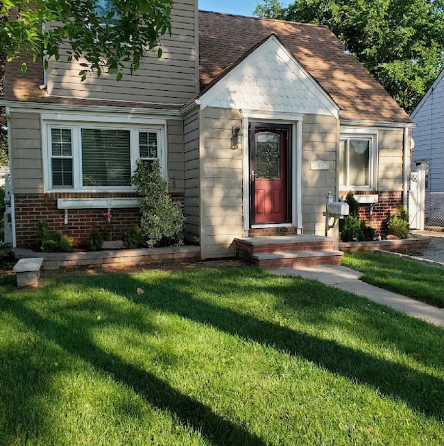 bungalow featuring brick siding, a front lawn, and roof with shingles