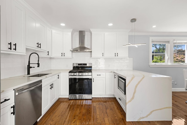 kitchen featuring appliances with stainless steel finishes, wall chimney exhaust hood, a sink, a peninsula, and white cabinetry