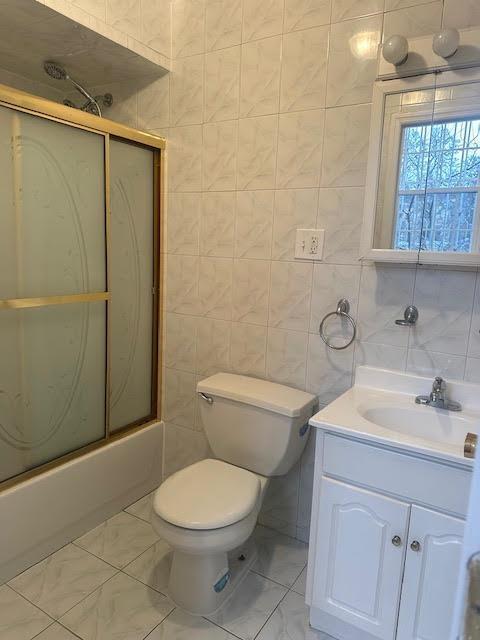 full bath featuring marble finish floor, tile walls, toilet, combined bath / shower with glass door, and vanity