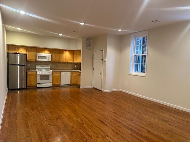 kitchen featuring dark wood-type flooring, white appliances, baseboards, and open floor plan