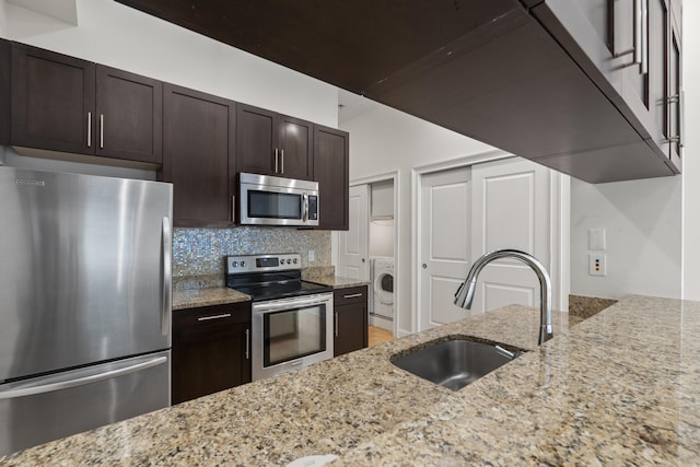 104 Tidewater St Unit 1A, Jersey City, NJ 07302 - kitchen featuring appliances with stainless steel finishes, washer / clothes dryer, light stone counters, dark brown cabinets, and backsplash