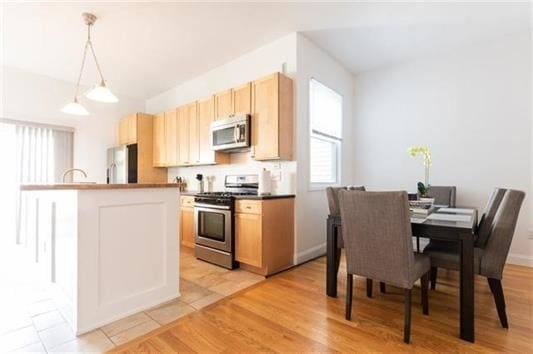 kitchen with a center island with sink, light brown cabinets, pendant lighting, stainless steel appliances, and light hardwood / wood-style floors