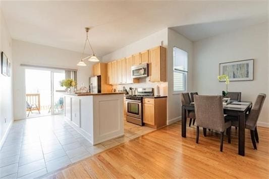 kitchen with pendant lighting, light brown cabinetry, light hardwood / wood-style flooring, and stainless steel appliances