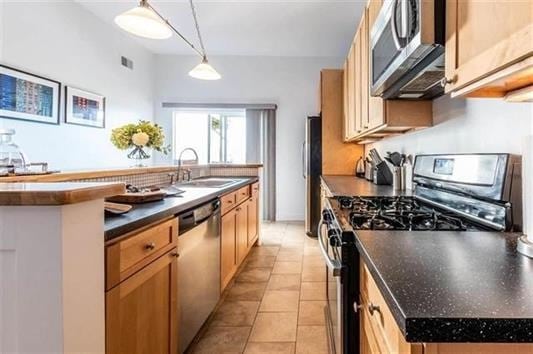 kitchen with sink, hanging light fixtures, light tile patterned floors, an island with sink, and stainless steel appliances