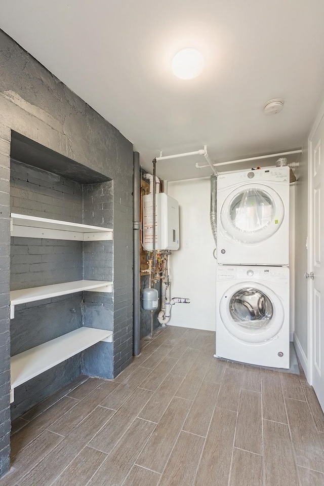 laundry room featuring stacked washing maching and dryer, water heater, laundry area, and wood finish floors