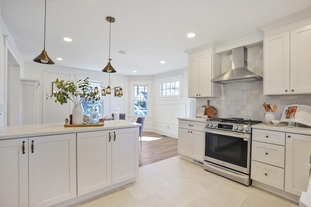 kitchen featuring decorative light fixtures, light countertops, backsplash, gas stove, and wall chimney exhaust hood