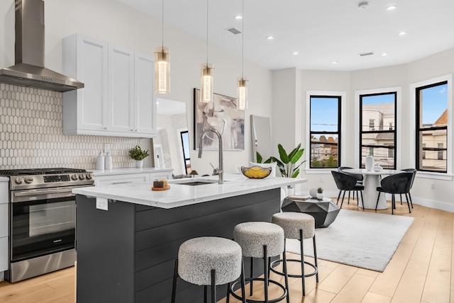 2602 Palisade Ave, Weehawken, NJ 07086 - kitchen featuring wall chimney range hood, stainless steel gas stove, a sink, light wood-style floors, and light stone counters
