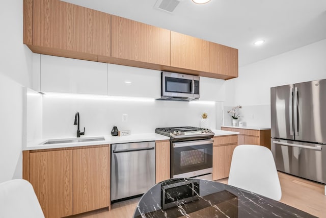 kitchen with light wood finished floors, visible vents, appliances with stainless steel finishes, a sink, and modern cabinets