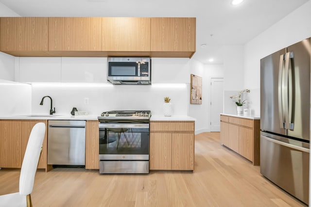 kitchen featuring stainless steel appliances, a sink, light countertops, light wood-type flooring, and modern cabinets