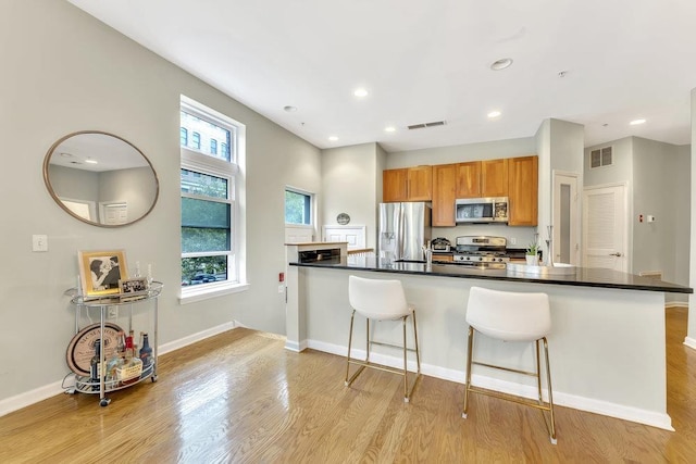1200 Grand St Unit 220, Hoboken, NJ 07030 - kitchen featuring appliances with stainless steel finishes, a kitchen breakfast bar, light wood-style floors, dark countertops, and brown cabinets