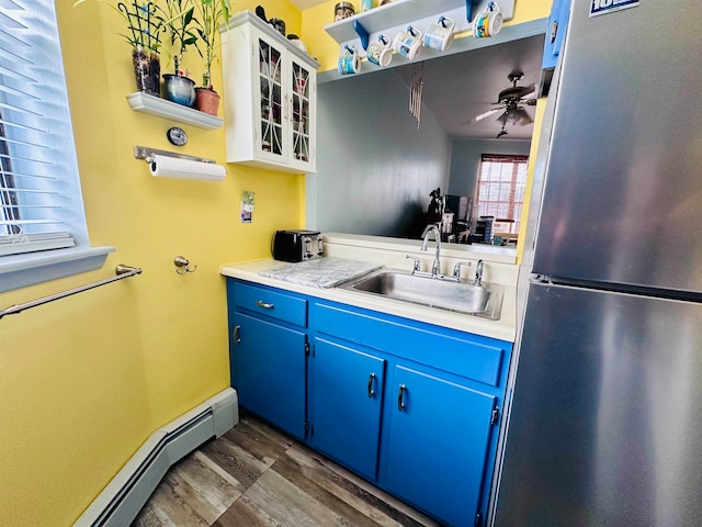 kitchen with a baseboard heating unit, stainless steel fridge, sink, white cabinets, and dark wood-type flooring