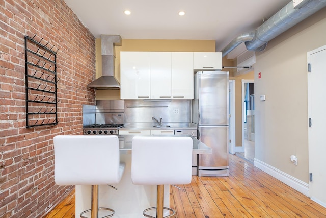 930 Park Ave Unit 3, Hoboken, NJ 07030 - kitchen with freestanding refrigerator, wall chimney range hood, brick wall, white cabinets, and light wood-style flooring