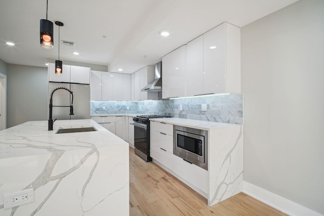 kitchen with sink, built in appliances, white cabinetry, hanging light fixtures, and wall chimney range hood