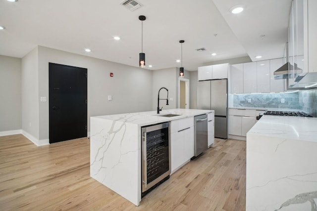 kitchen with beverage cooler, a kitchen island with sink, stainless steel appliances, pendant lighting, and white cabinetry