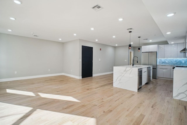 kitchen with white cabinets, light stone counters, a spacious island, stainless steel fridge, and pendant lighting