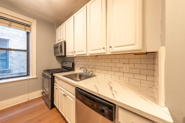 kitchen featuring light wood-type flooring, white cabinetry, a sink, backsplash, and stainless steel appliances