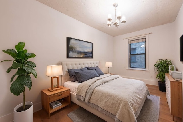 bedroom featuring an inviting chandelier, baseboards, and light wood-style floors