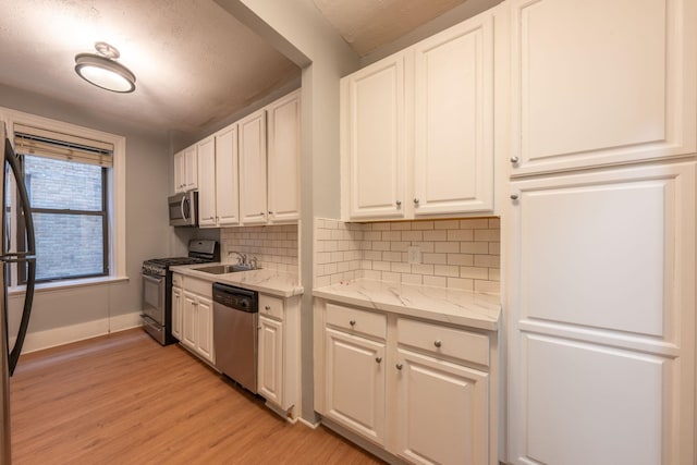 kitchen with baseboards, light wood-type flooring, tasteful backsplash, a sink, and appliances with stainless steel finishes