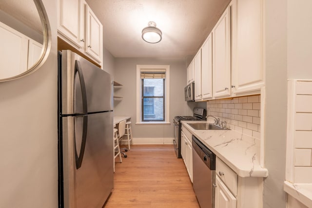 kitchen featuring decorative backsplash, appliances with stainless steel finishes, a sink, light wood-style floors, and white cabinetry