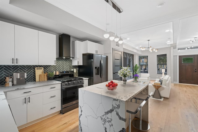 kitchen featuring a center island, decorative light fixtures, wall chimney range hood, white cabinets, and appliances with stainless steel finishes