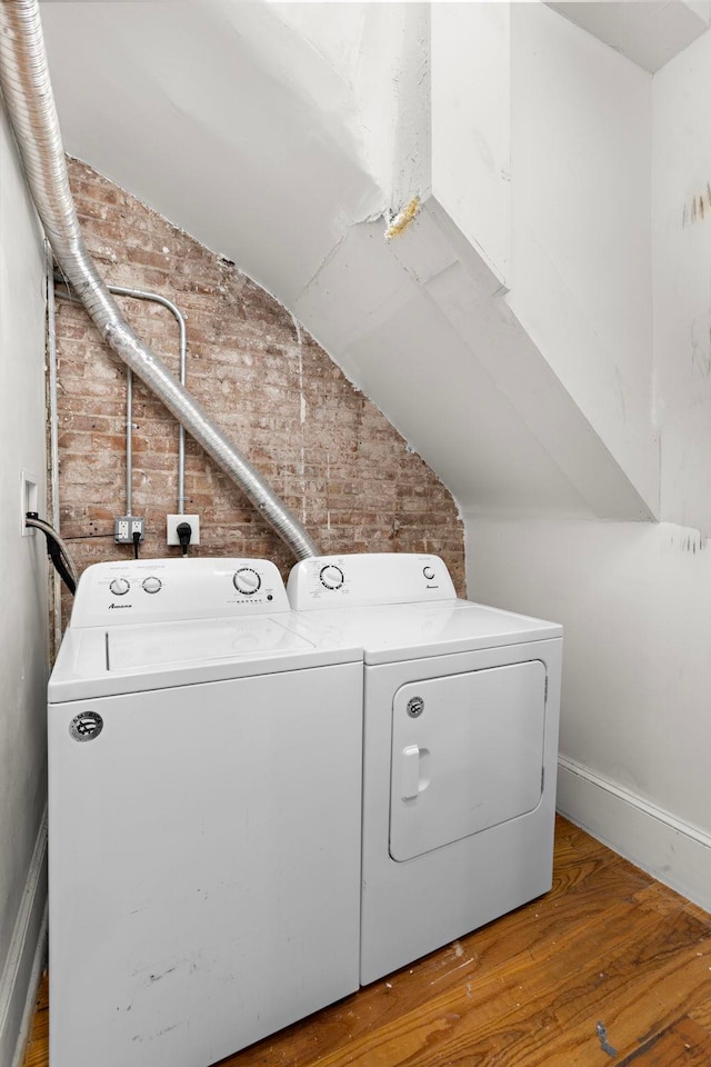 laundry area featuring washer and clothes dryer, hardwood / wood-style floors, and brick wall