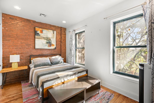 bedroom featuring wood-type flooring and brick wall