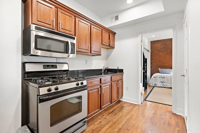 kitchen featuring light hardwood / wood-style floors, brick wall, sink, and appliances with stainless steel finishes