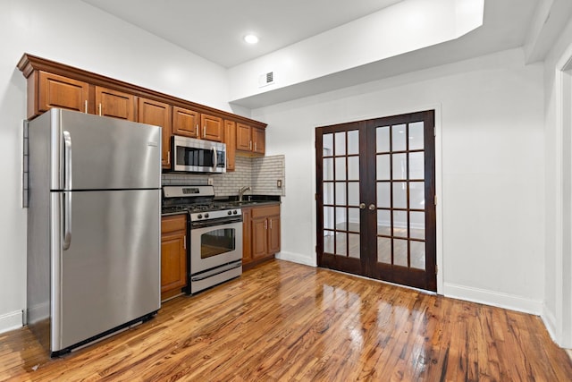 kitchen with tasteful backsplash, french doors, appliances with stainless steel finishes, hardwood / wood-style floors, and sink