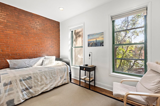 bedroom with multiple windows, hardwood / wood-style flooring, and brick wall