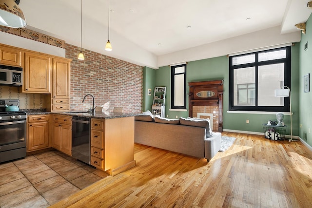 kitchen featuring dark stone counters, light wood-style flooring, appliances with stainless steel finishes, hanging light fixtures, and a sink