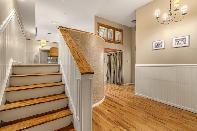 staircase with a chandelier, a wainscoted wall, and wood finished floors