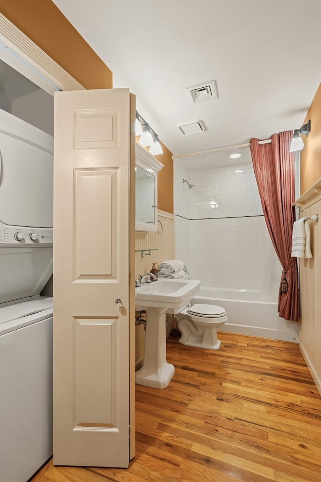 bathroom featuring shower / bath combination with curtain, toilet, wood finished floors, and stacked washing maching and dryer